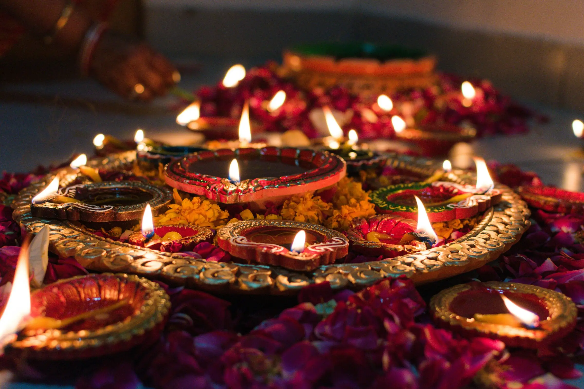 Copper diyas and marigold petals arranged on a dark surface